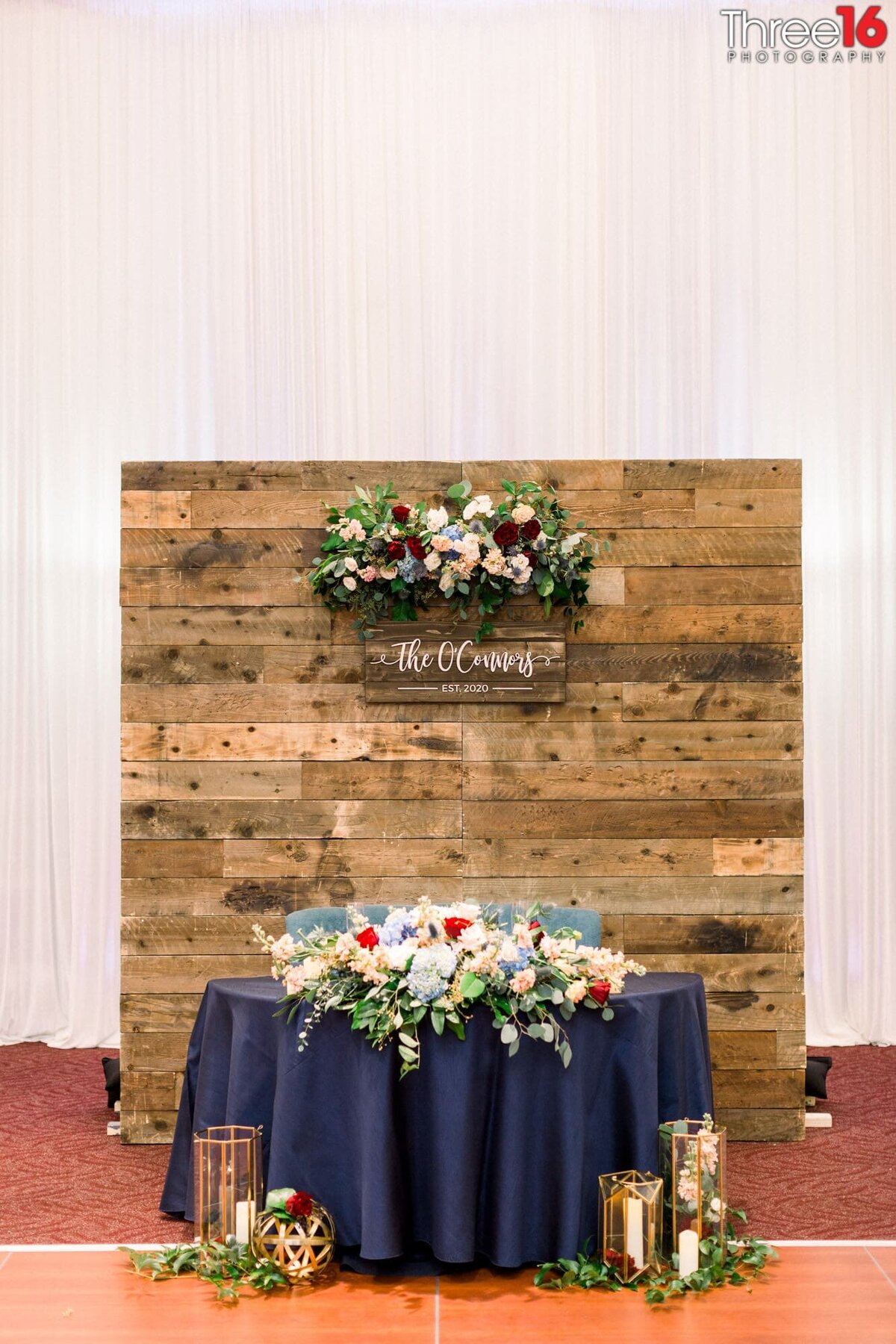 Sweetheart table decked out with flowers and a wood-backed wall