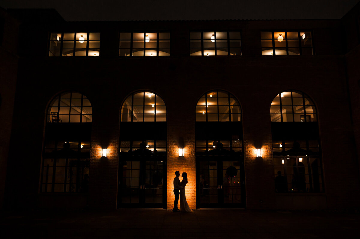 A bride and groom is silhouetted in front of the courtyard at Revel Motor Row in Chicago, Illinois