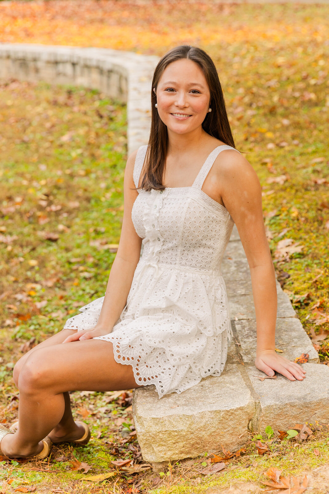 senior girl wearing a white dress sitting on a wall in a Atlanta park by Laure photography