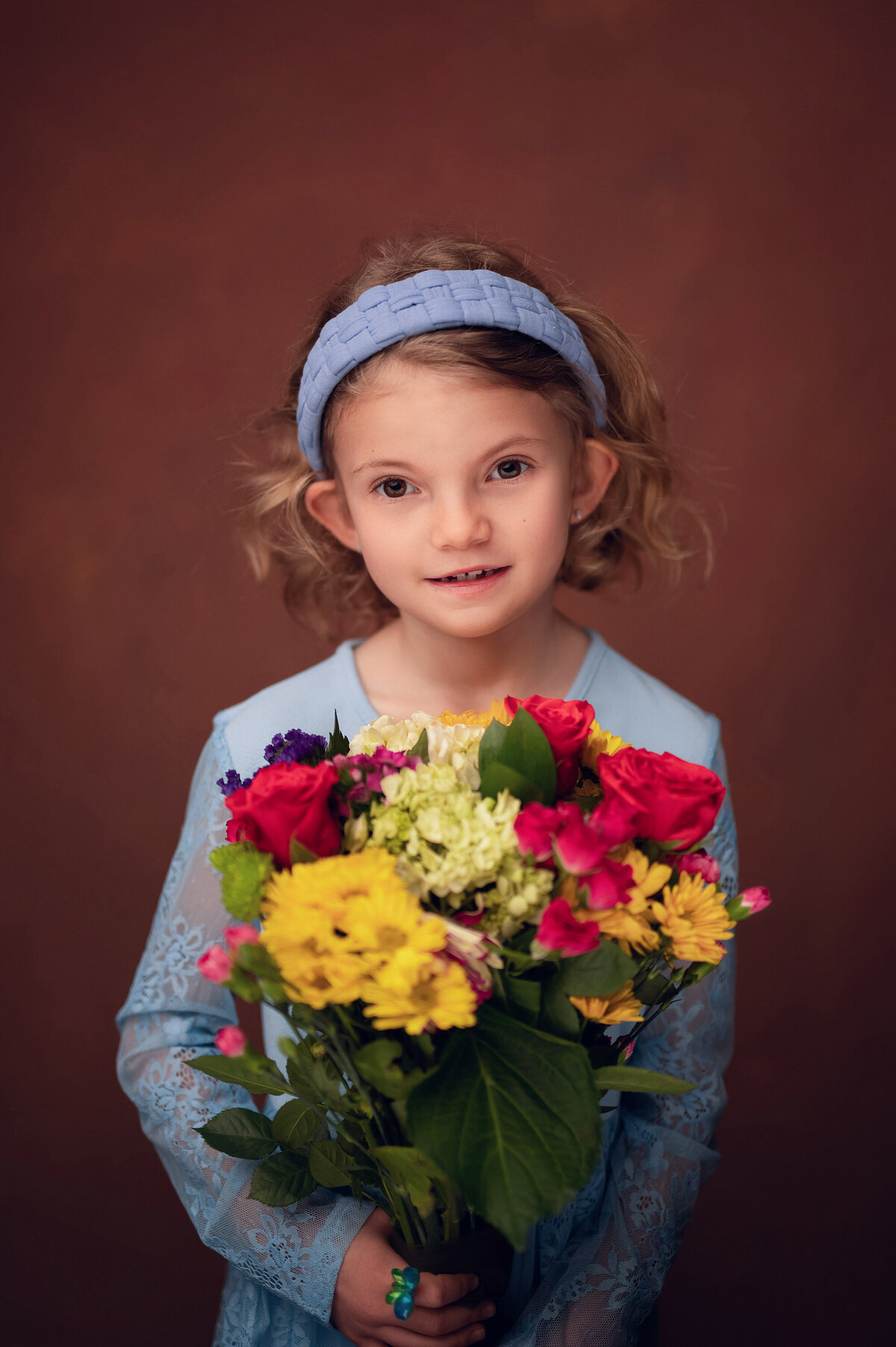A young girl dressed all in periwinkle holds a bouquet of flowers in our Waukesha portrait studio.