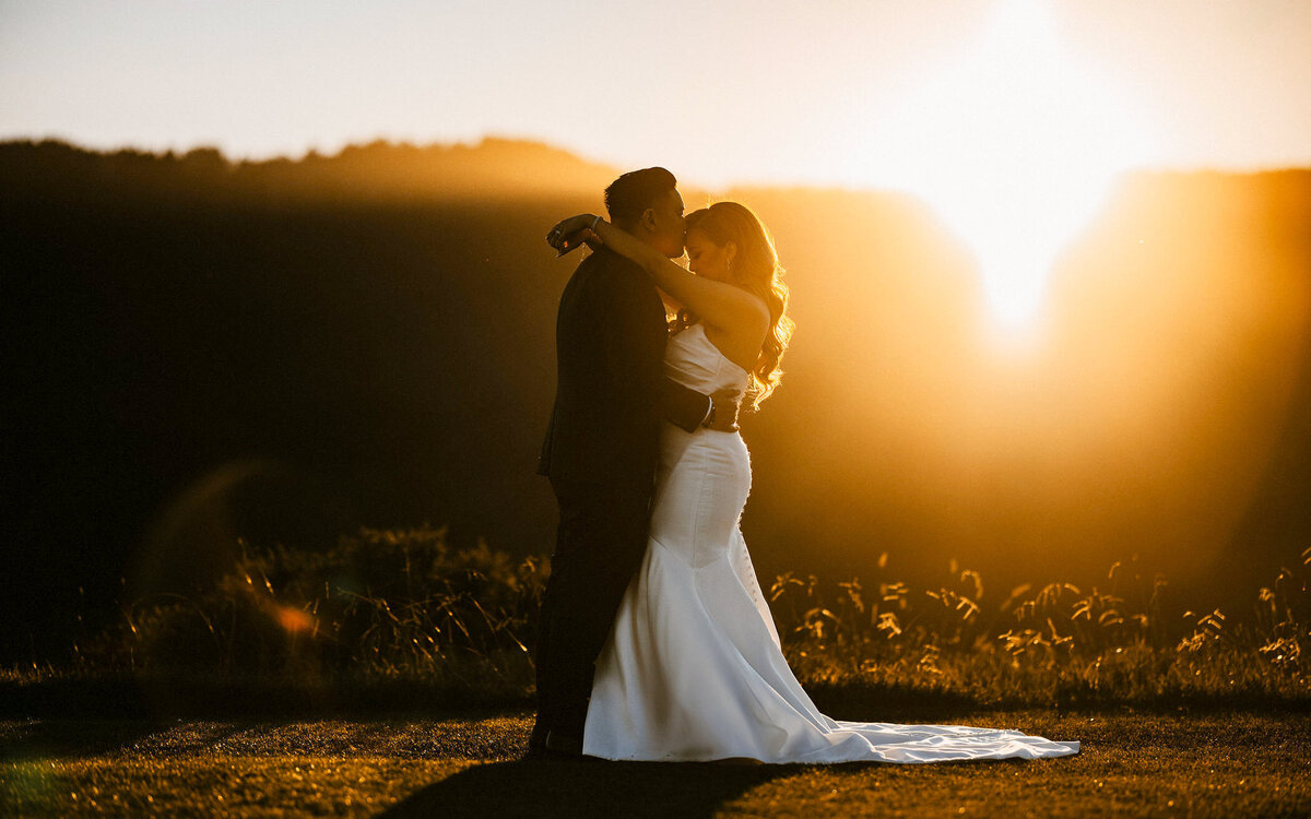  Bride and groom kiss at sunset, an example of the golden light and cinematic style we bring to Asheville weddings in the Blue Ridge Mountains.
