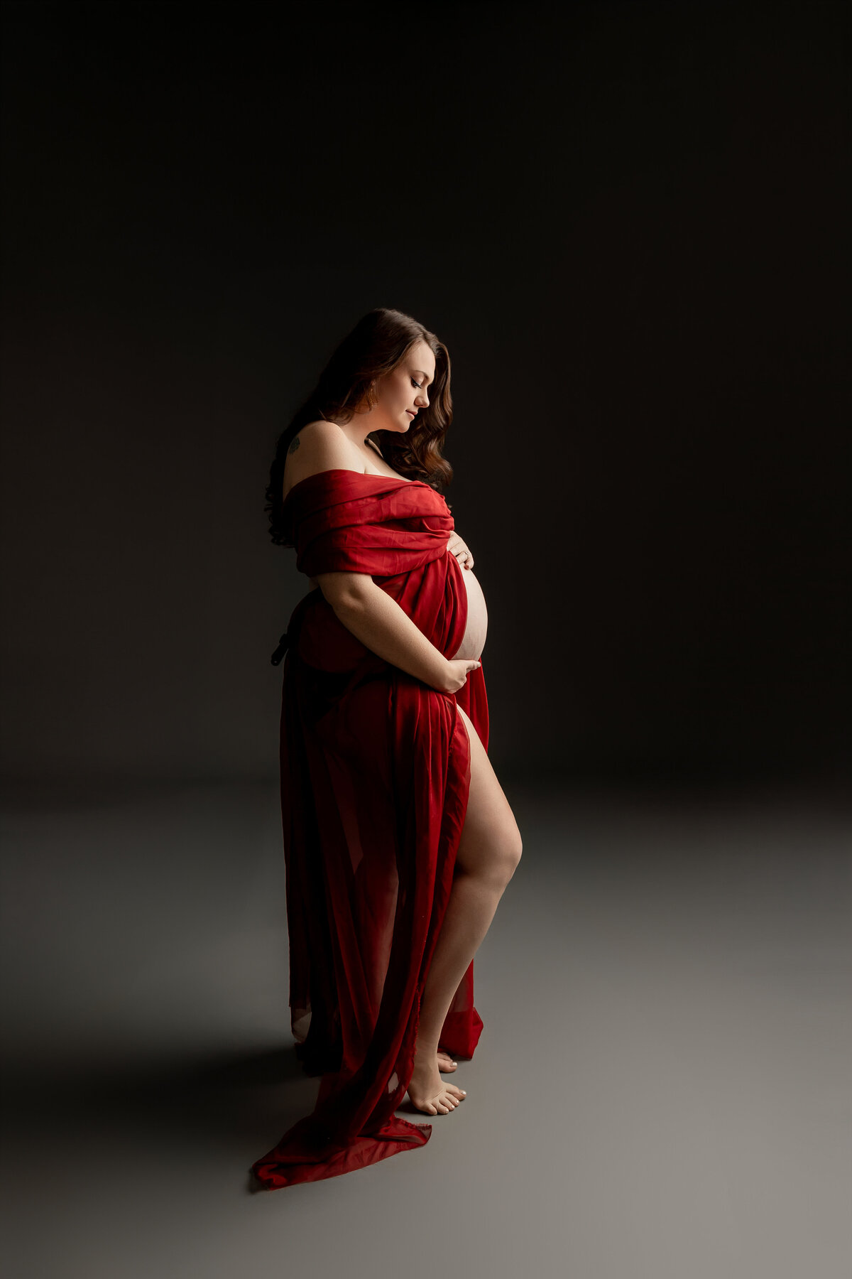 Dressed in a vibrant red dress, she stands poised in a side view. Captured by Inland Empire maternity photographer Kaitlyn Dawn Photography.