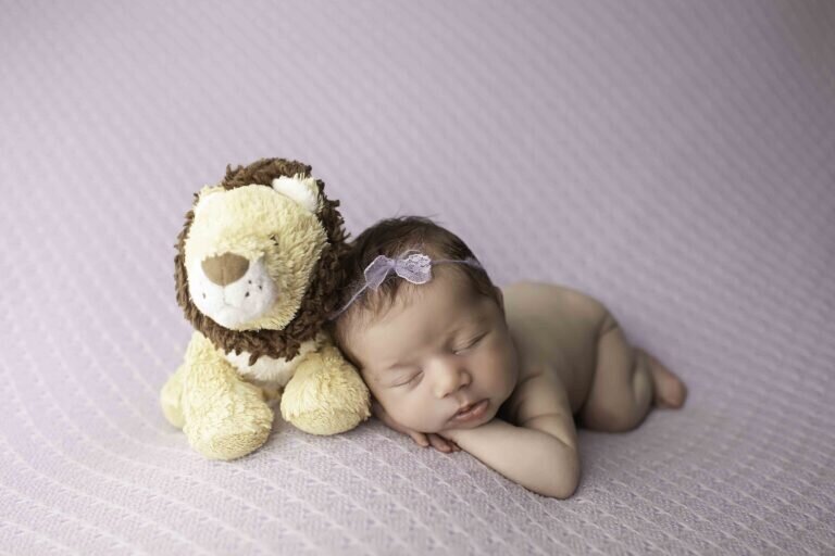 Newborn baby peacefully resting while snuggled up with a small plush lion, creating a sweet and cozy scene