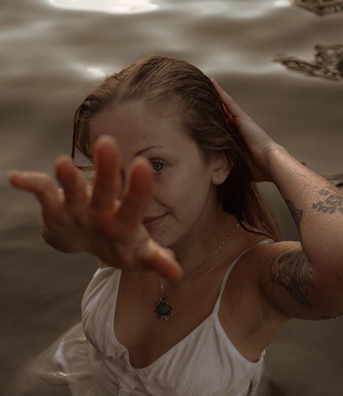 woman wearing white dress stands in the river and holds her hand close to the camera, creating an artistic photo