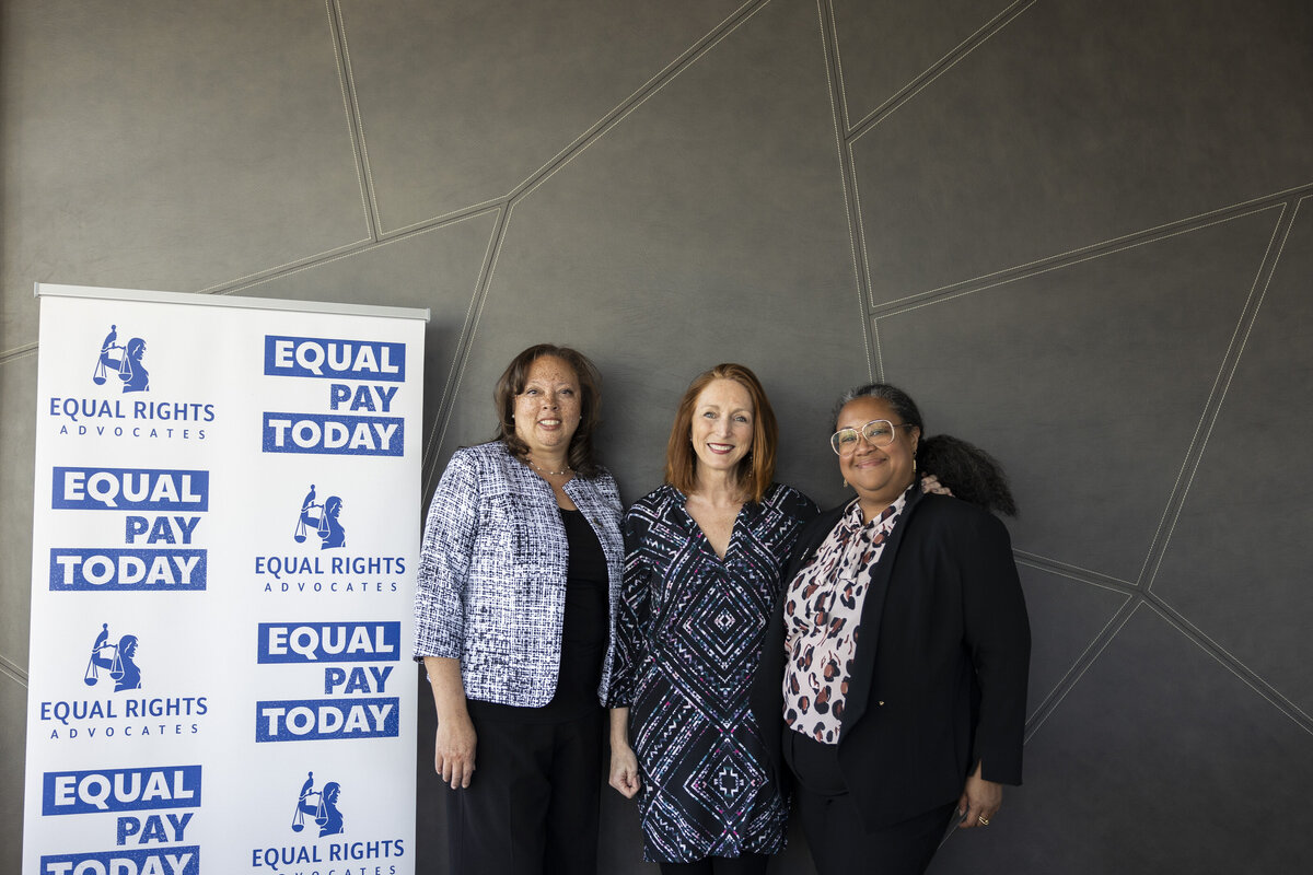 Three people pose next to a sign that says Equal Pay Today.