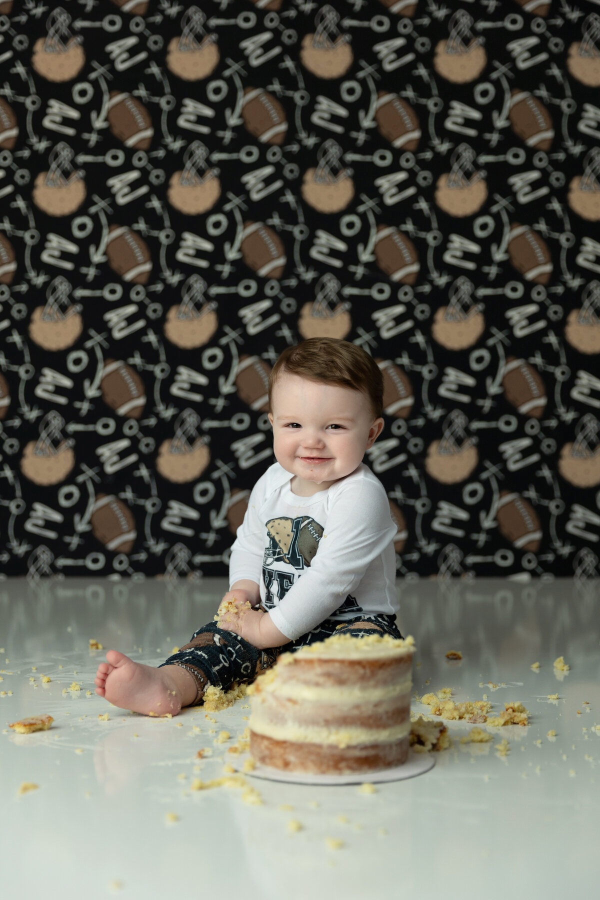 A happy toddler boy smiles while sitting on a studio floor surrounded by cake