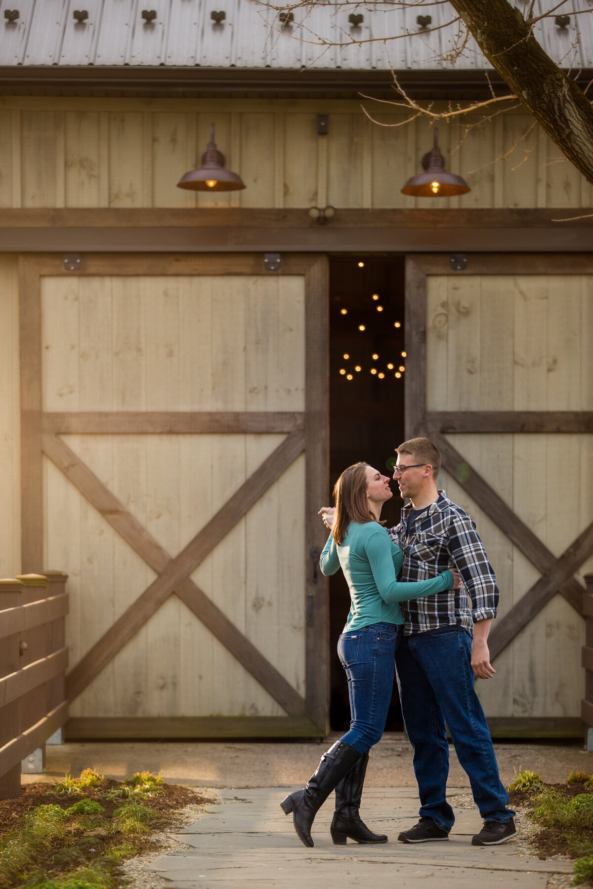 Rustic engagement photo of a couple sharing an intimate moment outside a weathered barn, bathed in warm, natural light and surrounded by countryside charm.