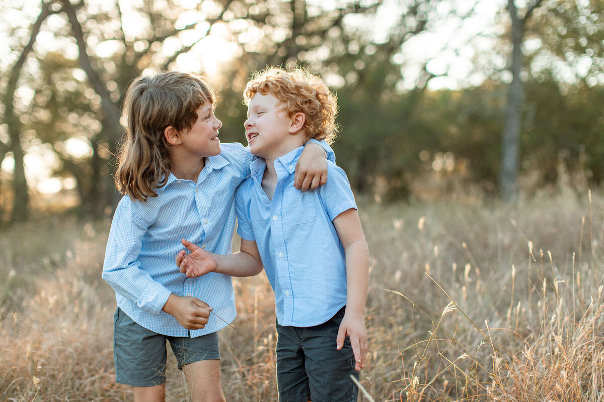 Two children playing in a sunlit field, photographed by Sara James, a family photographer in San Antonio.