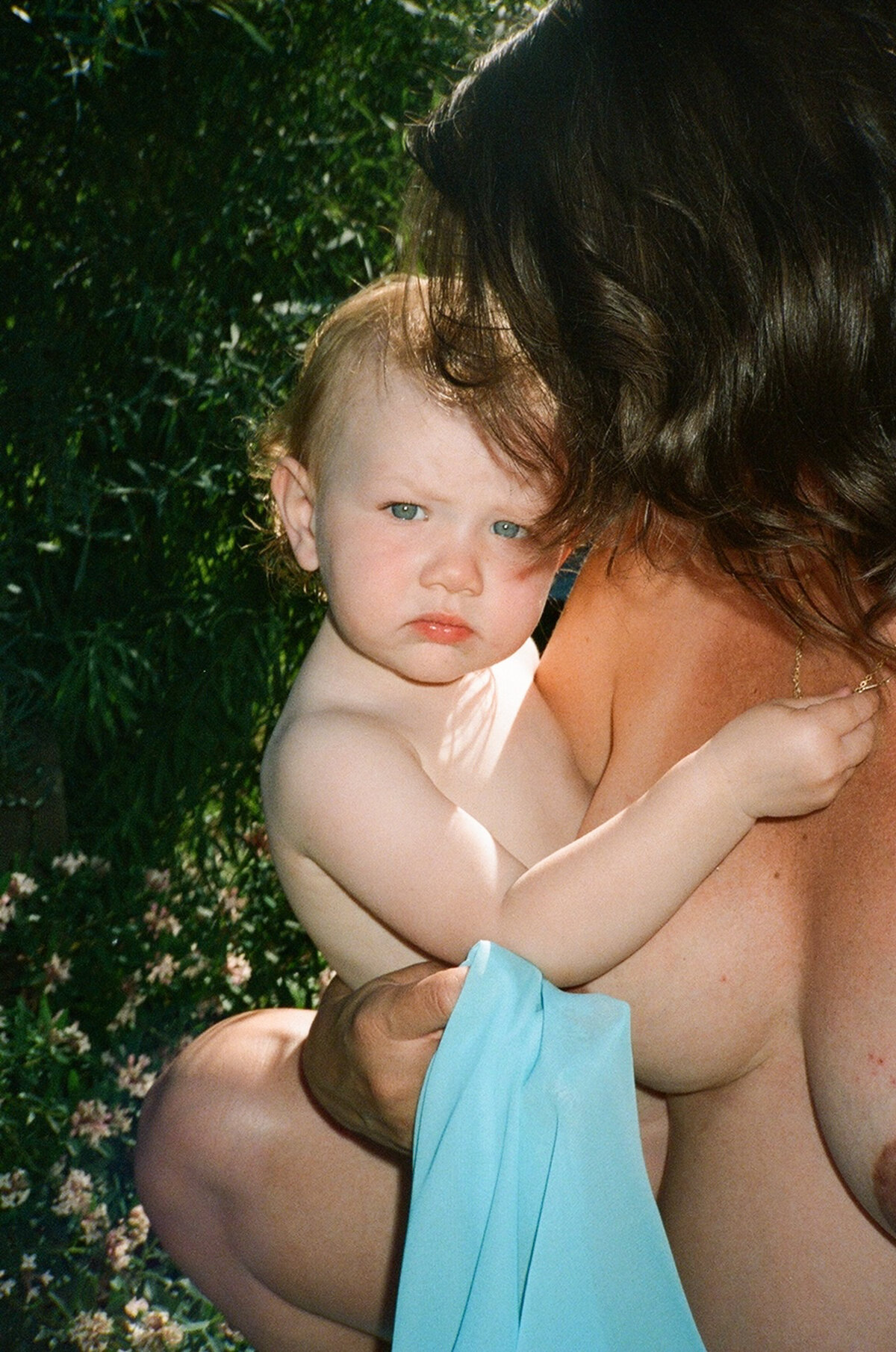 Color film photograph of toddler daughter in mother's arms in summer sunlight