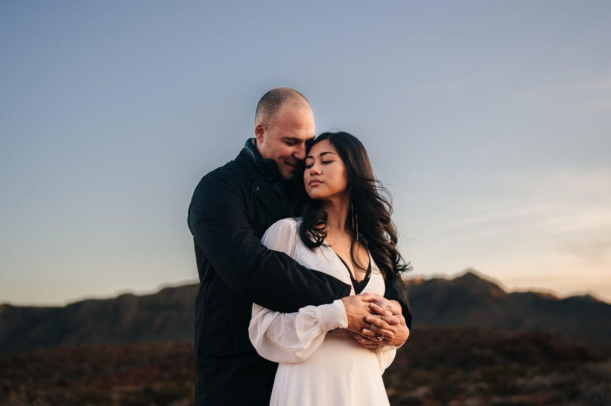 A tender elopement moment at Valley of Fire in Las Vegas, as the groom lovingly embraces the bride from behind, surrounded by the natural beauty of this unique desert landscape.