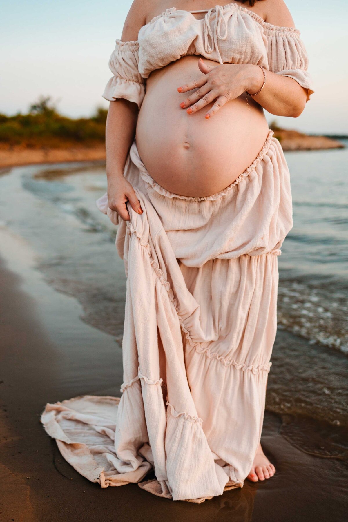 The professional photographer in Albuquerque captures a stunning maternity scene with the future mom in a light pink outfit, standing gracefully in front of the sea.