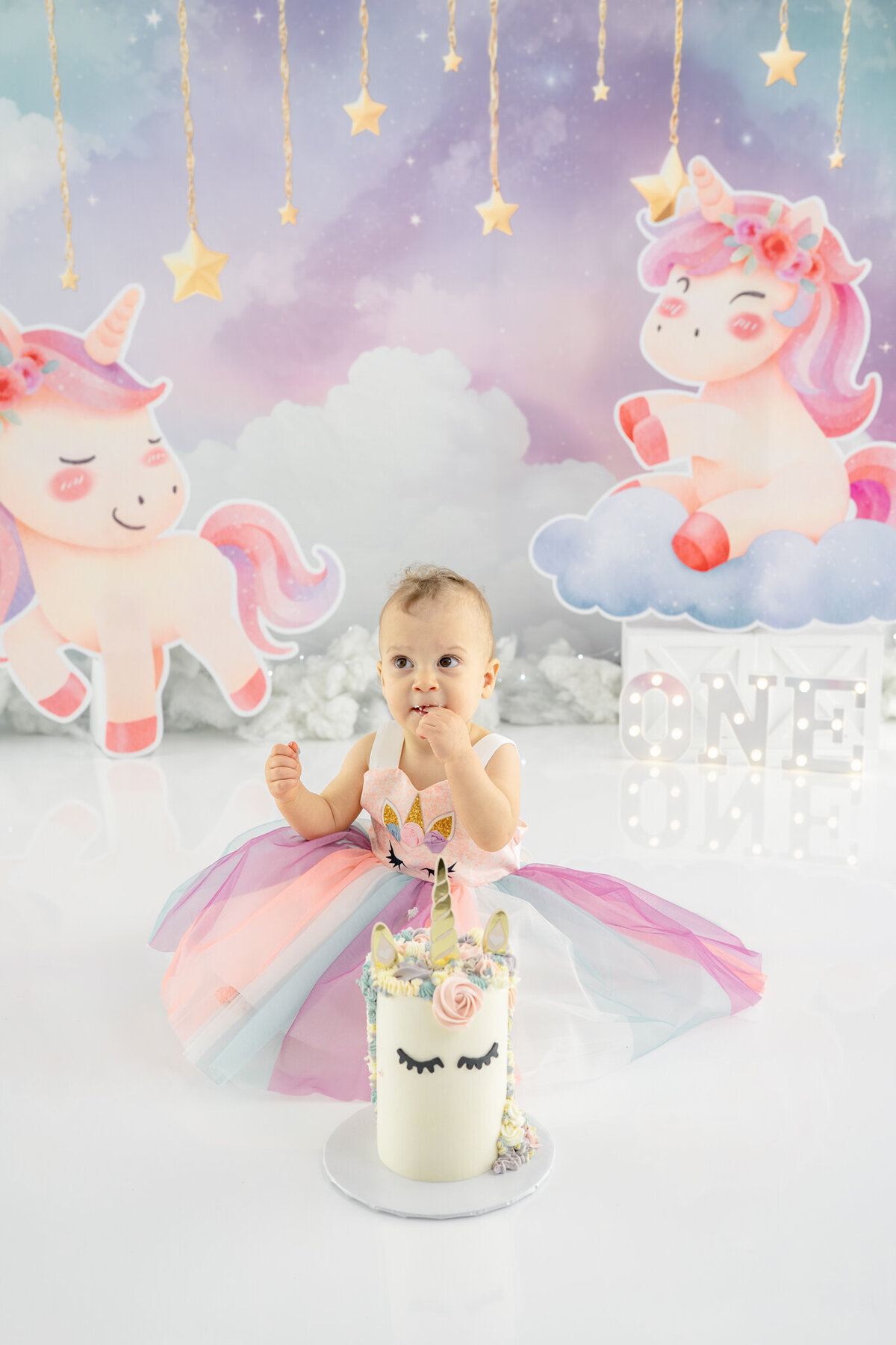 Girl in unicorn dress eating unicorn cake during themed cake smash session— captured by Alliston and Barrie cake smash photographer.