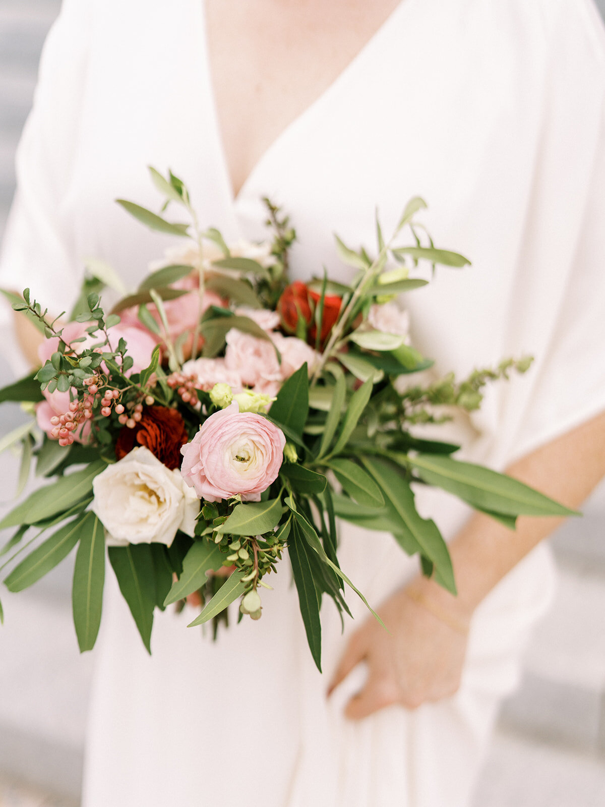 Sweet bridesmaid bouquet comprised of greenery, pinks and pops of red flowers featuring ranunculus, garden roses and pepper berry. Floral Design by Rosemary and Finch in Nashville, TN.