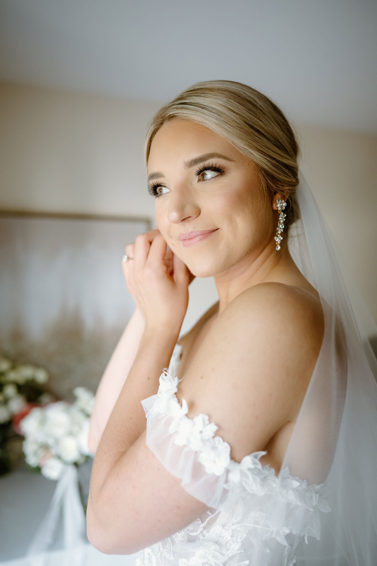 Bride getting ready, wearing floral lace gown and crystal drop earrings.