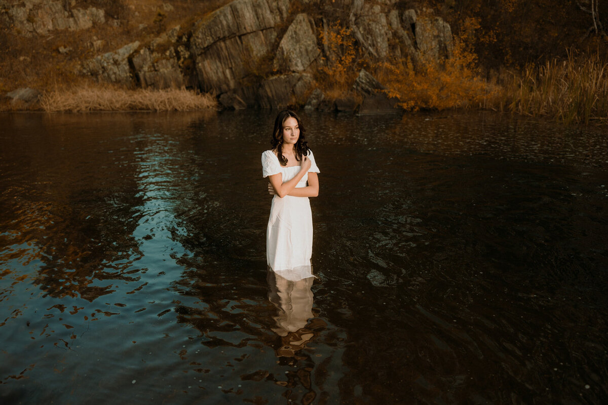 Senior wearing a white dress standing in a creek near Rapid City
