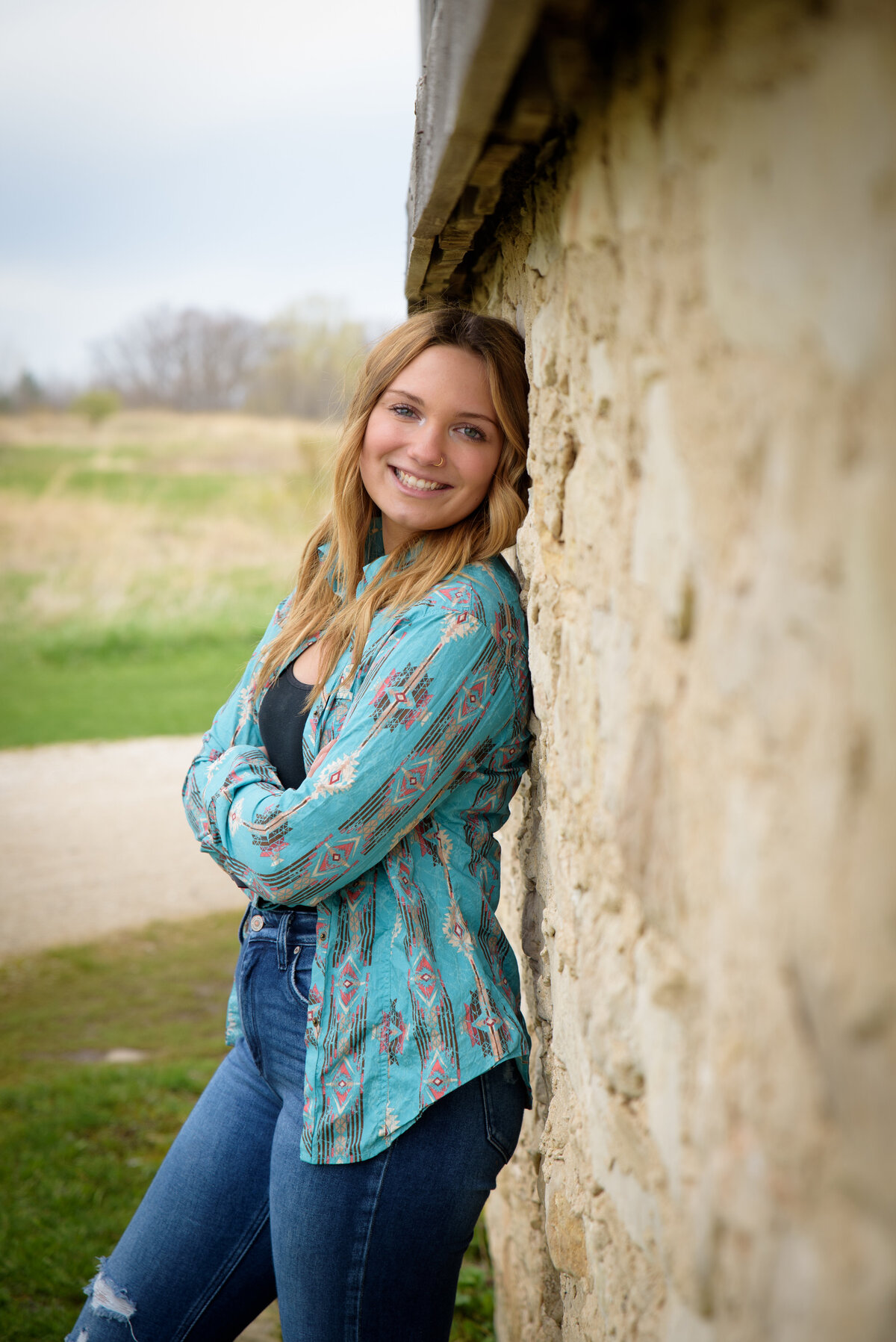 high school senior girl leaning against stone wall of barn at Fonferek Glen County Park in Green Bay, Wisconsin