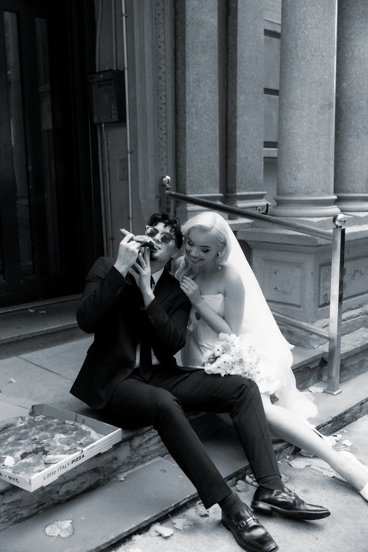 Bride and groom sharing a romantic moment while splitting a slice of pizza in NYC.