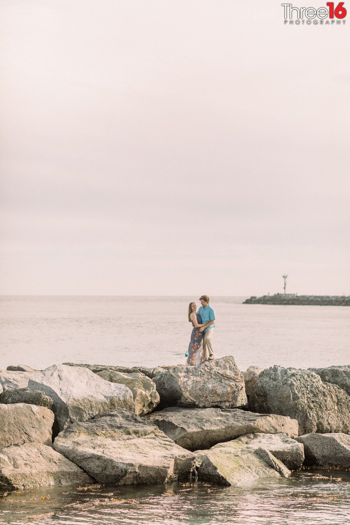 Engaged couple pose together on the jetty of Corona del Mar State Beach
