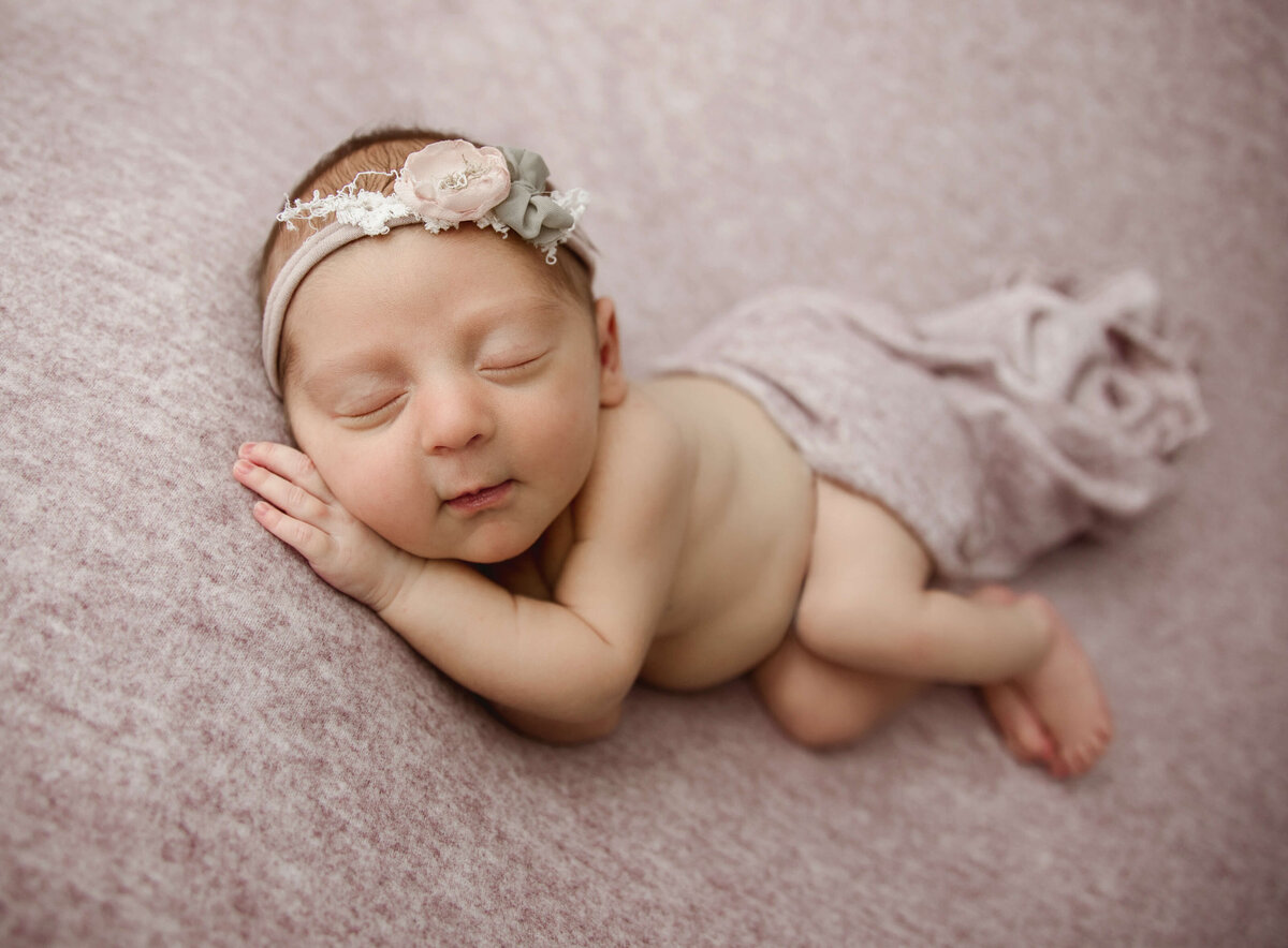 Picture of a newborn baby girl posed on her side on a pink blanket