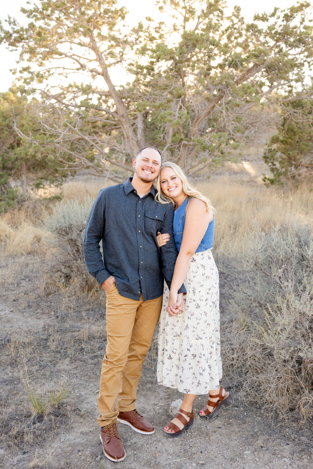A couple stands together in a natural setting, holding hands and smiling. Their warm embrace and happy expressions capture the essence of their deep connection.
