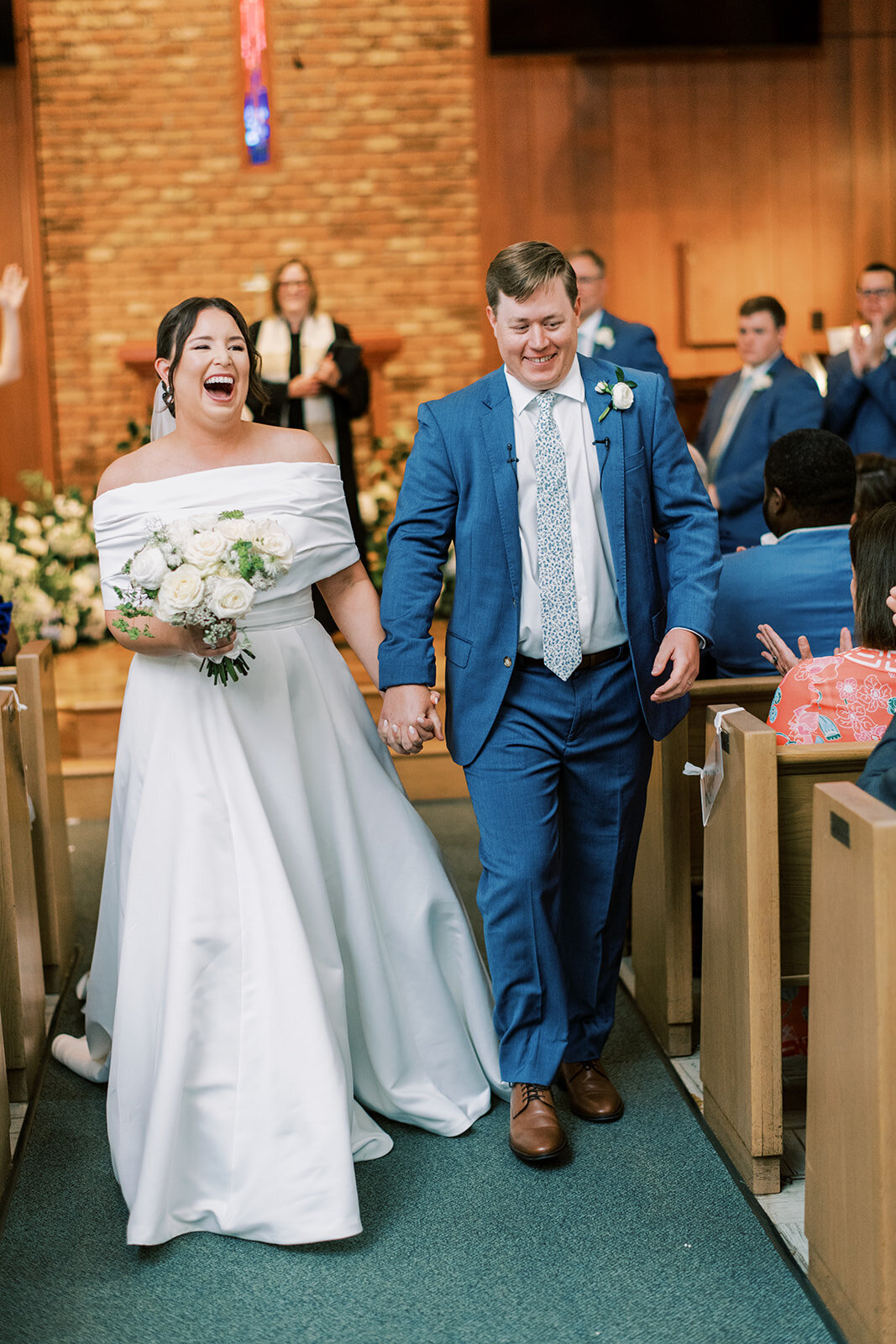:
 Newly married couple walking up the aisle smiling after ceremony at Cashiers United Methodist Church.
