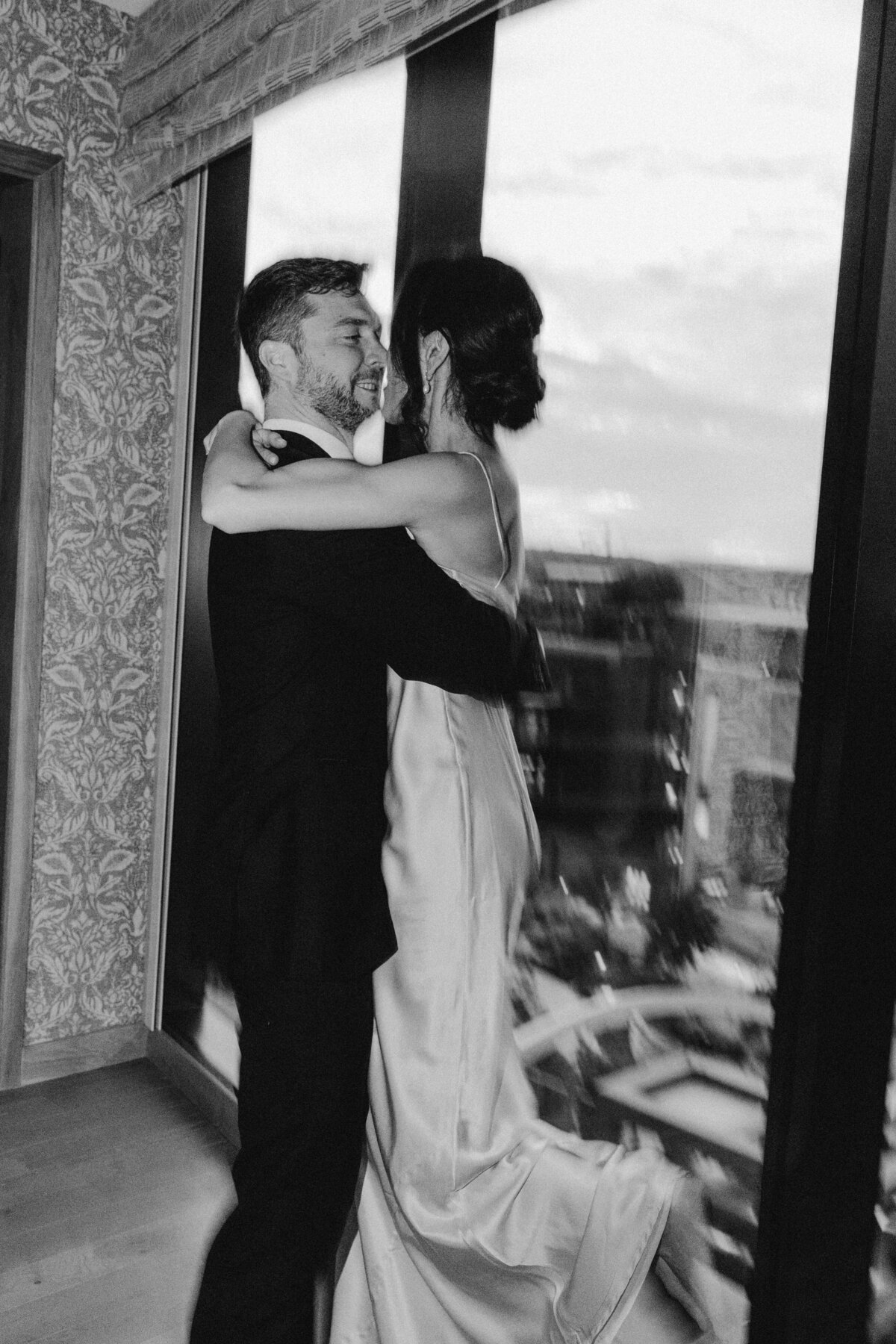 Bride and groom embracing by large windows overlooking the city of Austin