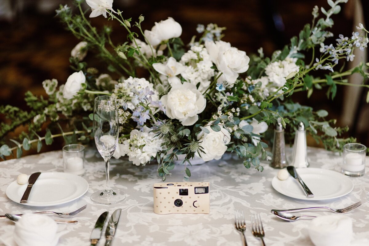 White floral centerpiece with greenery at a wedding reception.