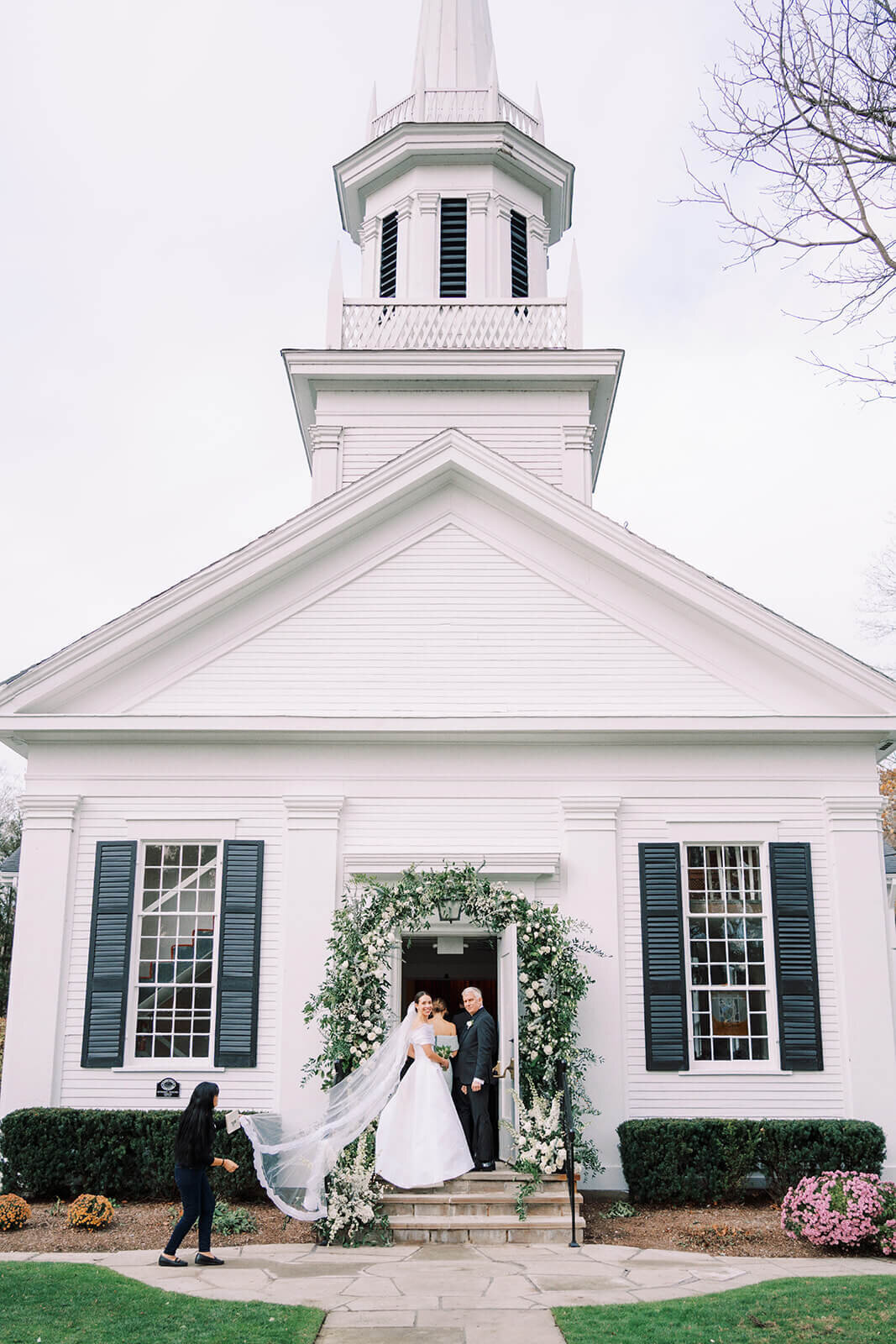 20. Bride and groom exiting a white chapel under a lush green and white floral arch.