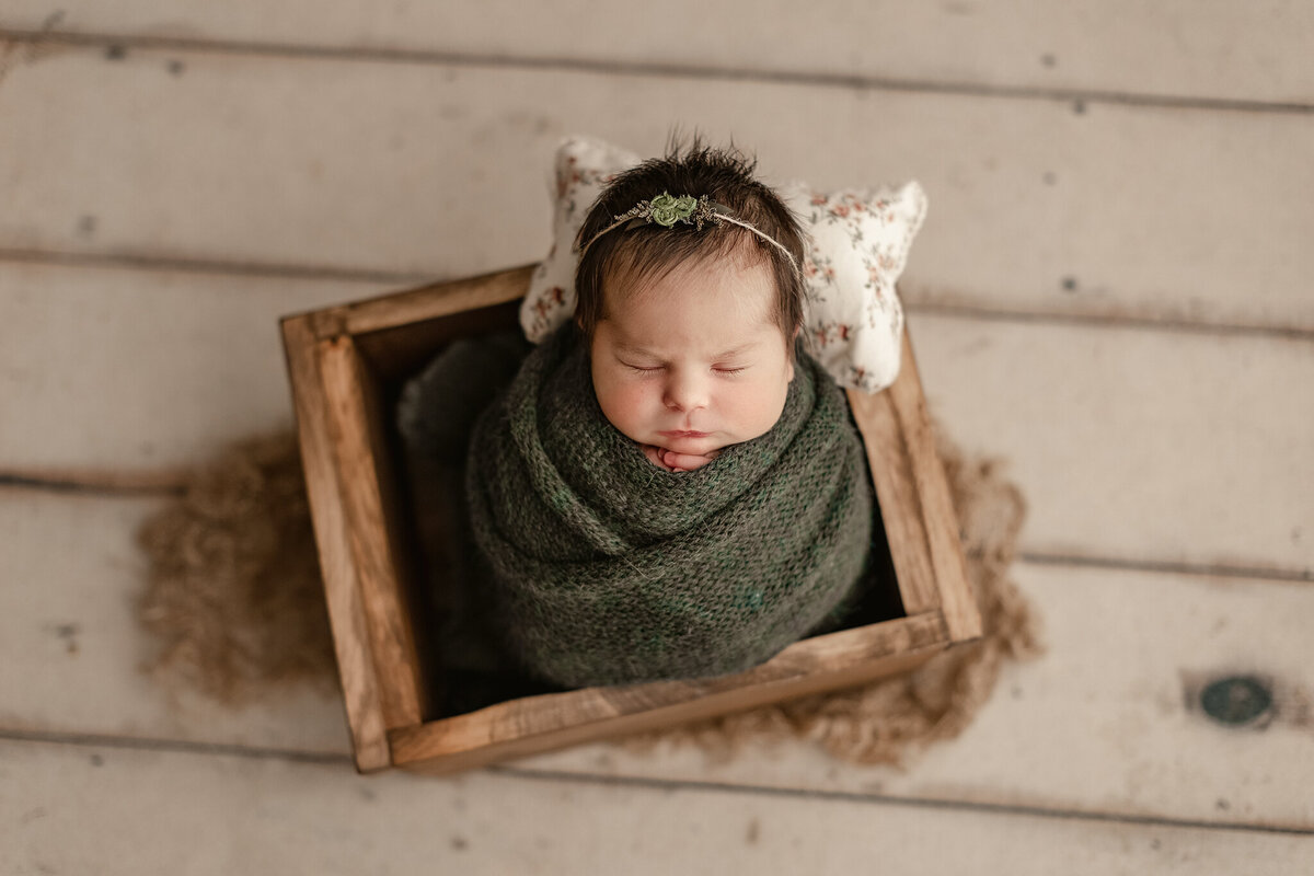 baby girl swaddled in a green wrapped in a wood crate in our denver newborn photography studio