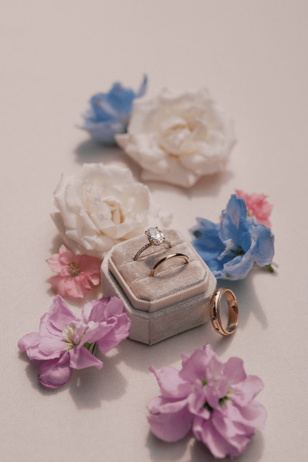 Wedding rings styled with pastel flowers on soft linen at a summer wedding at Moonlight Basin, featuring an oval diamond engagement ring and gold bands.