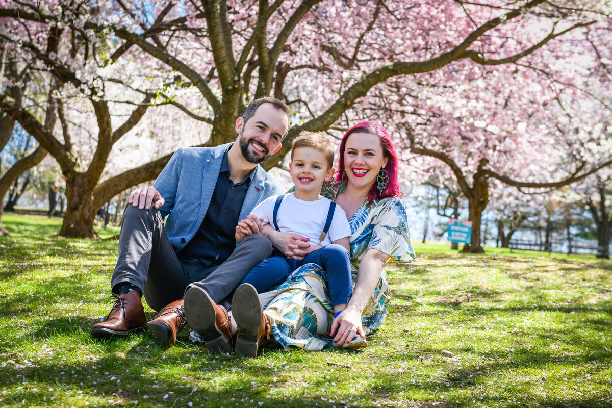 Two parents sitting in the grass with their child sitting in their lap