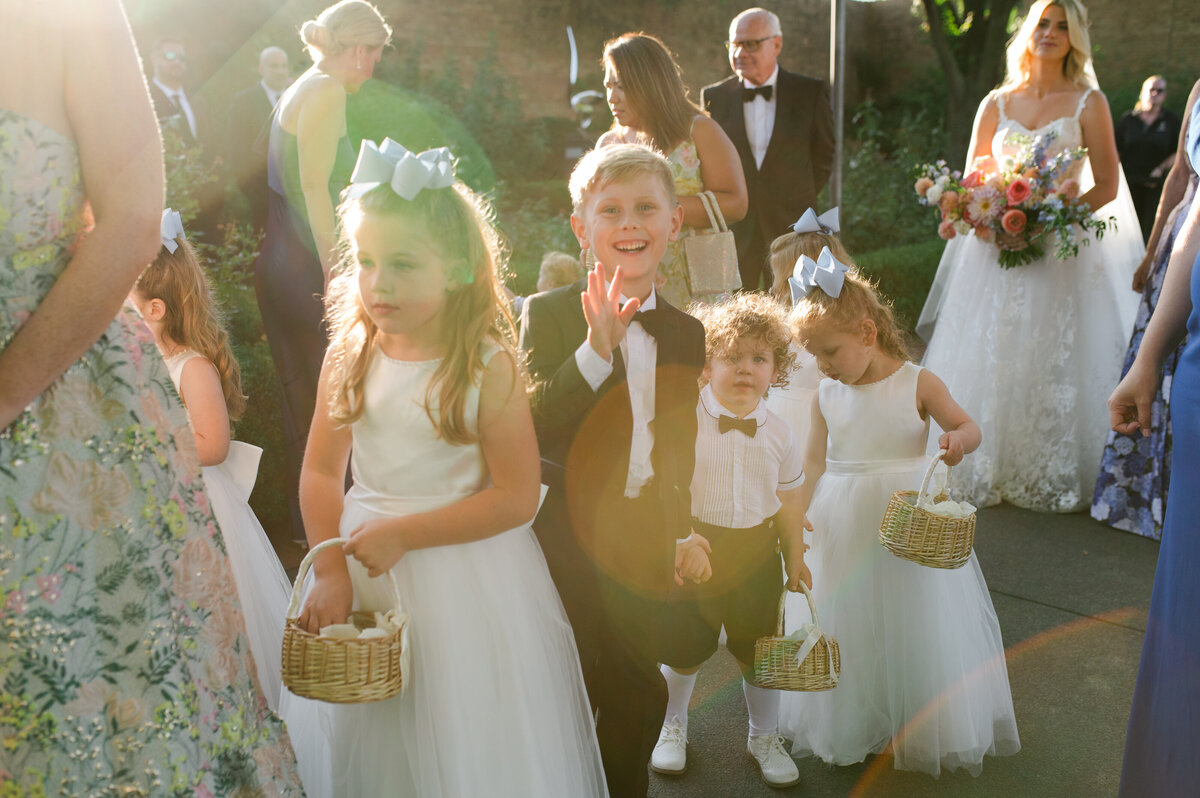 Young ring bearer and flower girls walking down the aisle in white outfits at the Chicago Botanic Gardens.