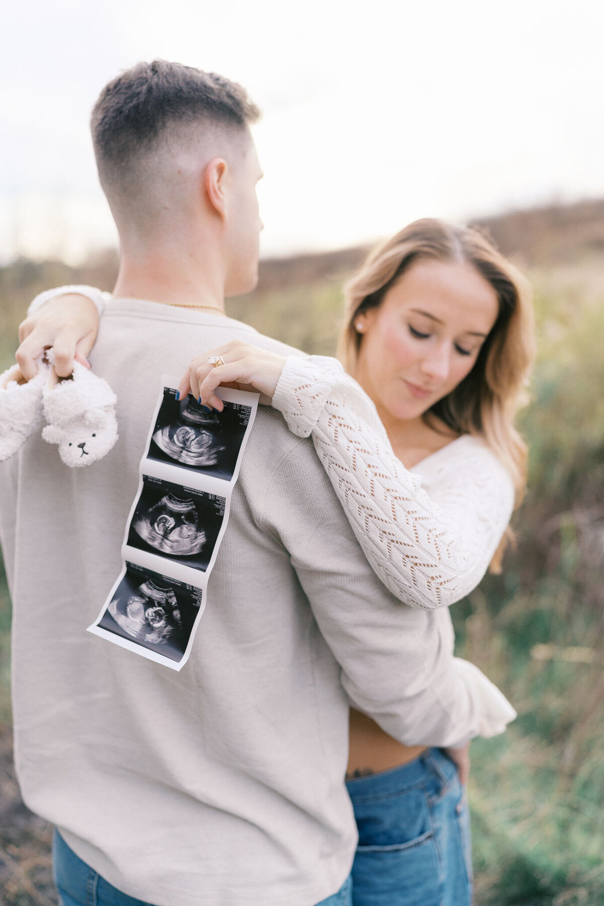 man holds pregnant wife's belly and holds ultrasound during golden hour in knoxville tennessee