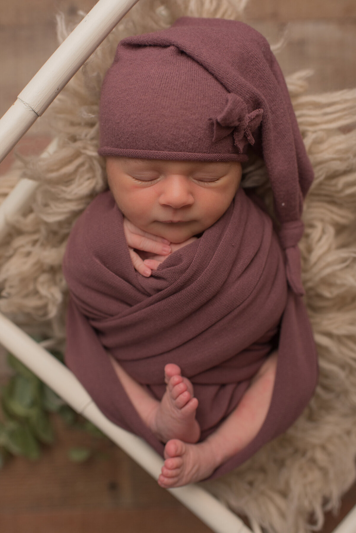 Newborn baby girl wearing purple wrap and hat with bow