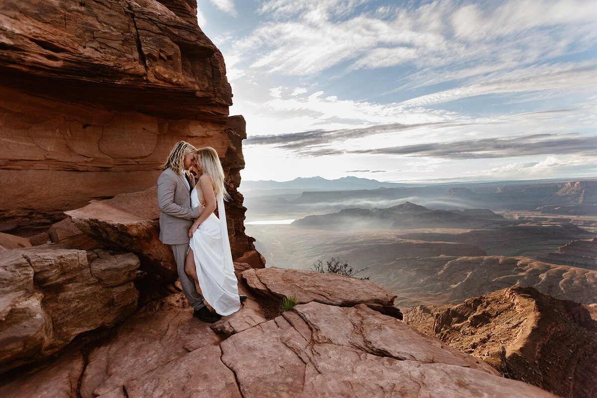 A couple tightly embraces during their elopement in Utah. It is misty over the mountains adding drama.
