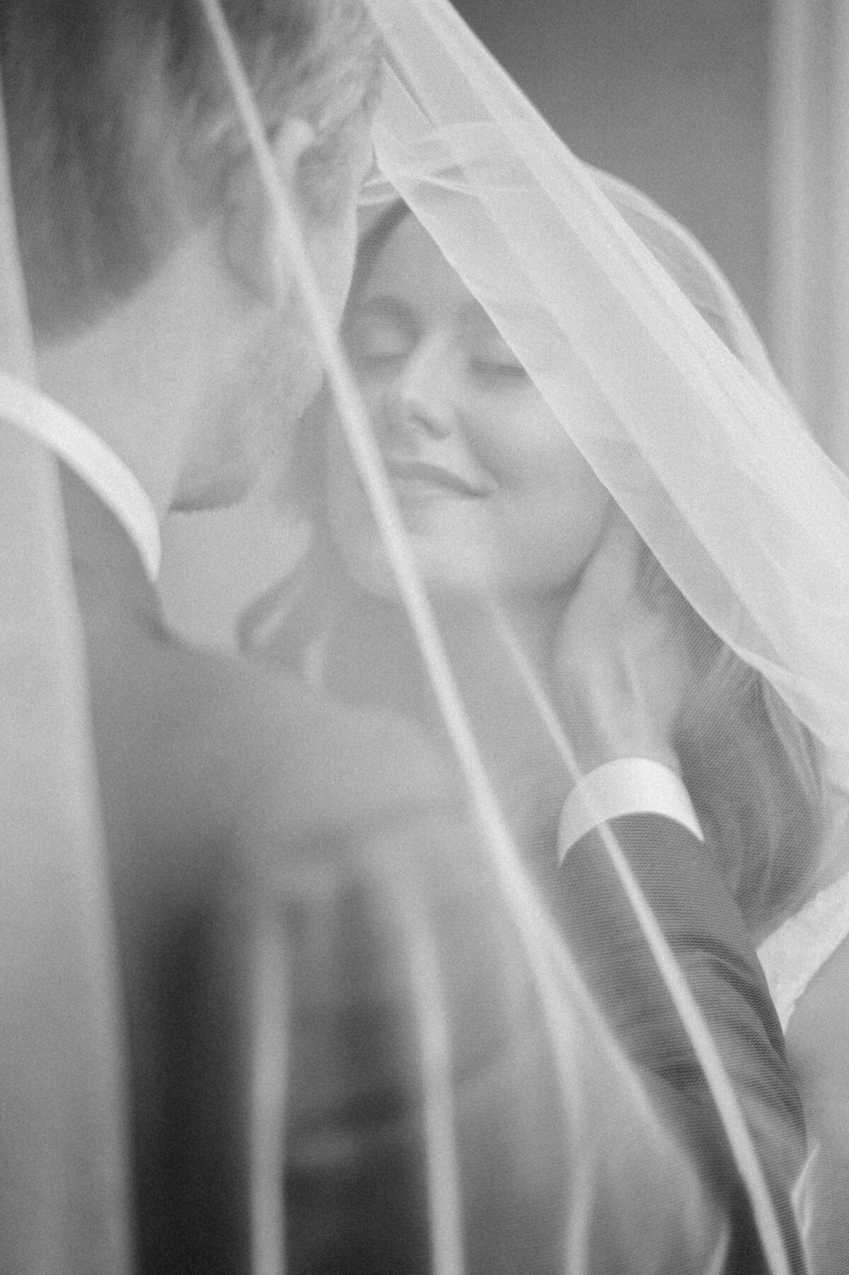 Groom looks into brides eyes under a veil. Holding her neck. Bride is smiling.