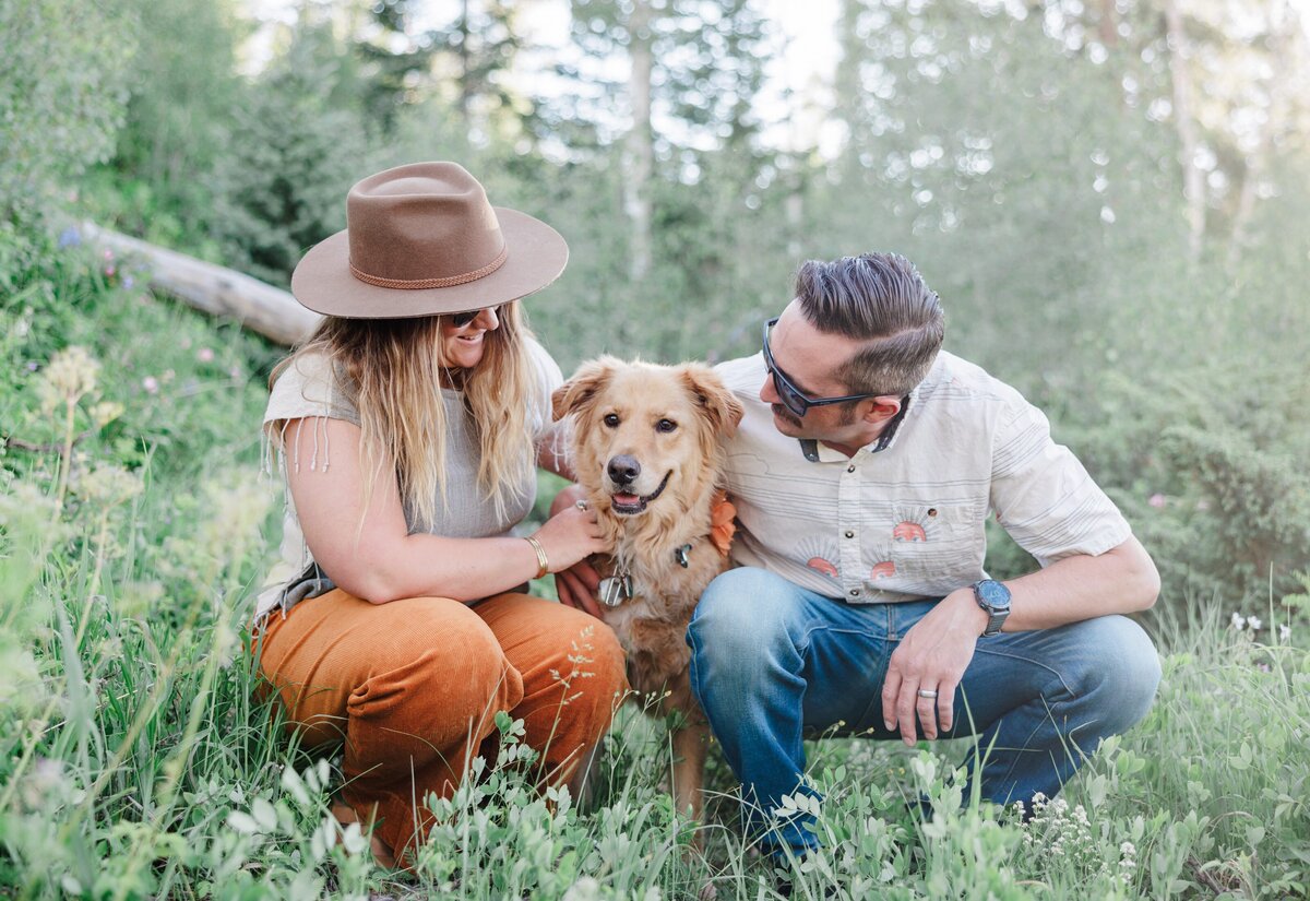 A brown dog is hugged by mom and dad in a forest at sunset during a Breckenridge Couples Photography session