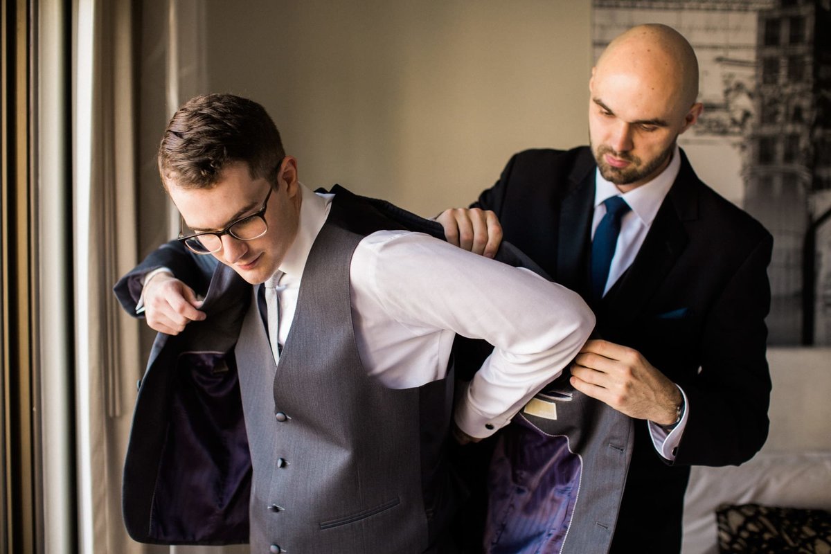 Best Man helps the Groom putting on his suit jacket prior to the wedding