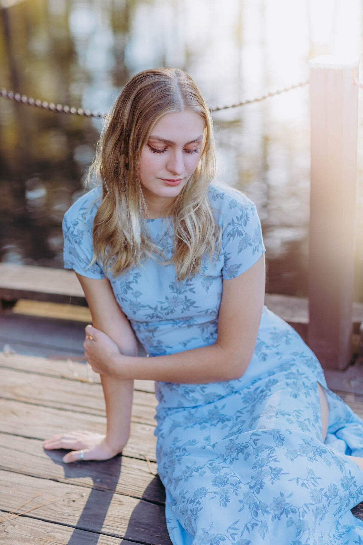 A girl sitting on the dock looking down with the sun flowing in behind her.