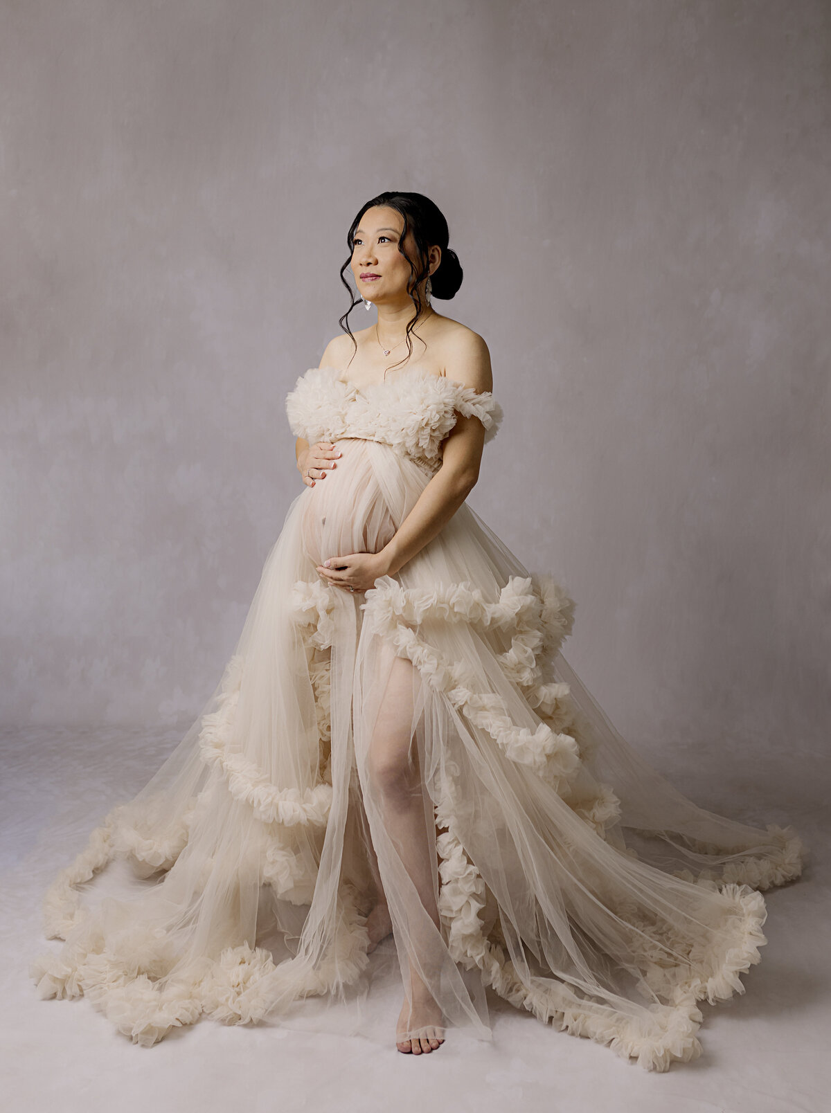 pregnant mother in cream dress holding belly looking away from camera