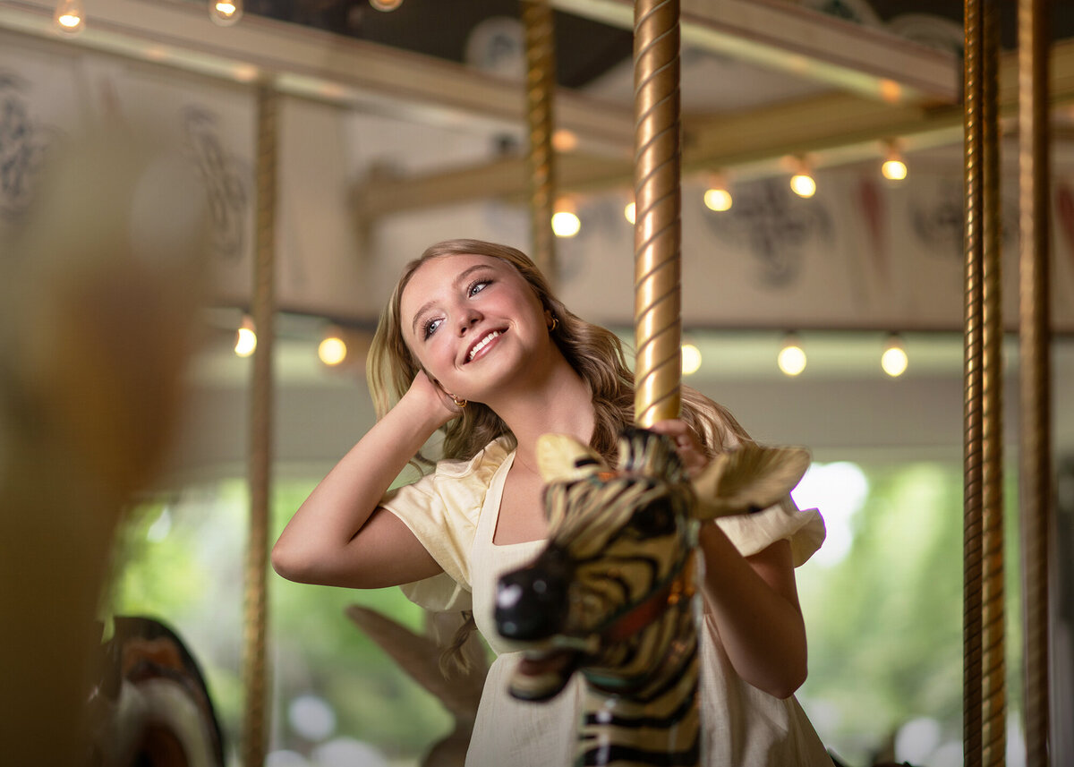 A high school senior rides a Zebra on a carousel in a white dress