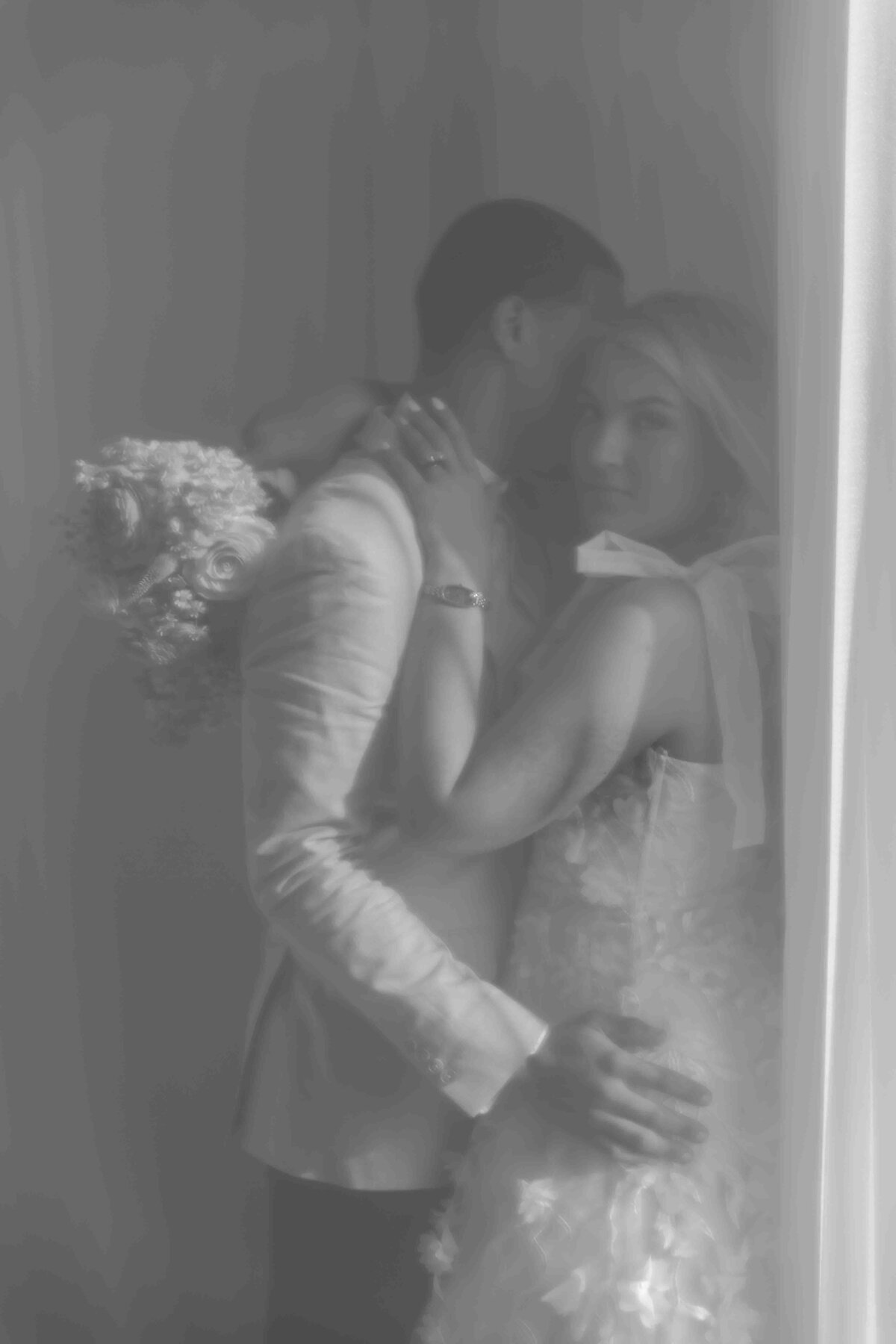 bride and groom standing against a wall through white curtain in black and white