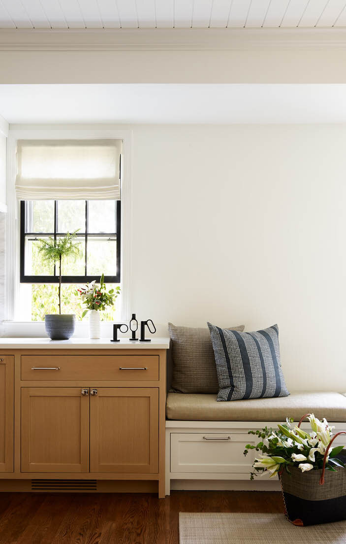 Explore the kitchen in a historic Hingham home, where a series of lower white cabinets at the end of the oak cabinets create a cozy window seat, providing extra seating for the casual dining area.