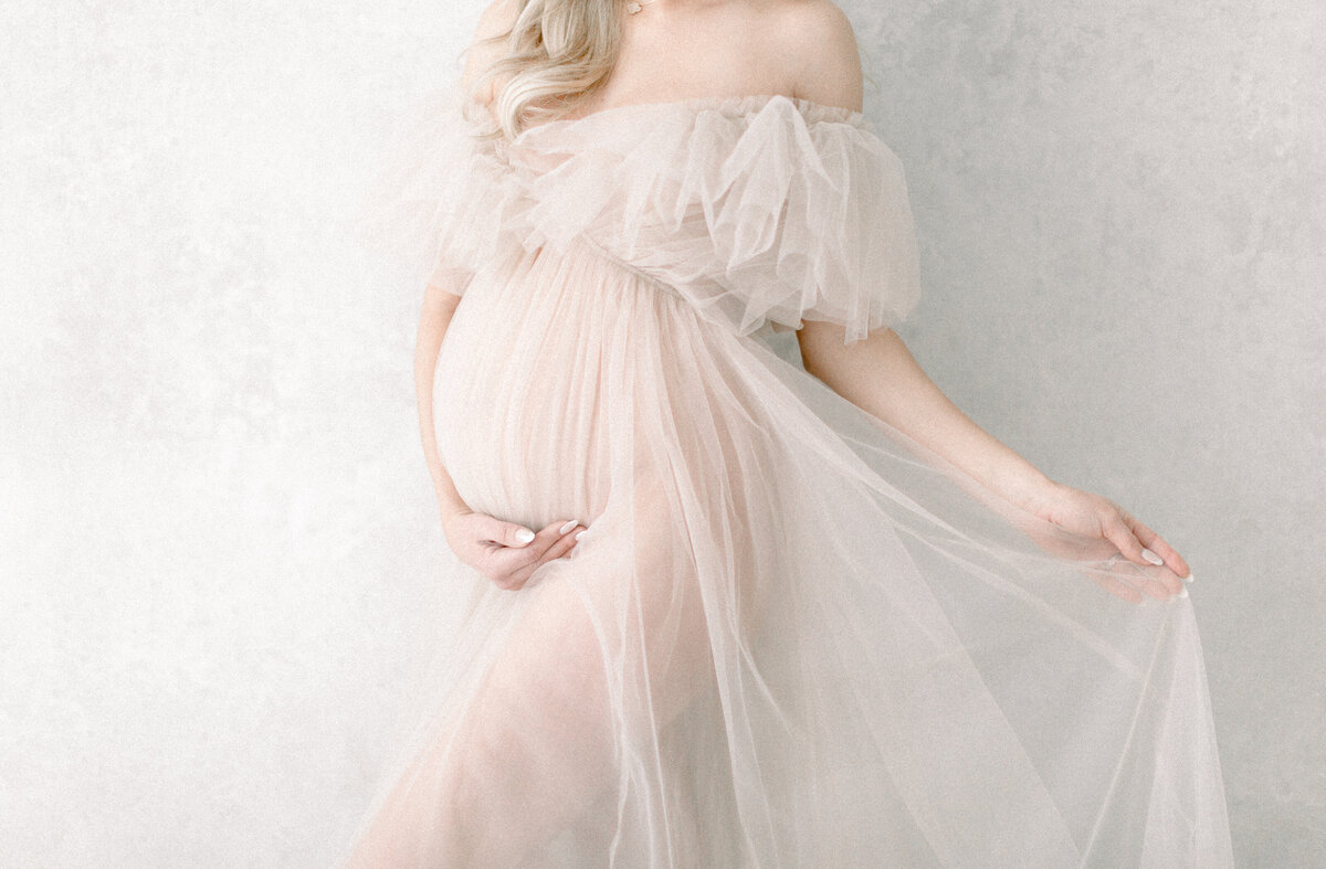 A maternity photoshoot in a Las Vegas photo studio of a mother dressing in a tulle maternity gown holding her belly.