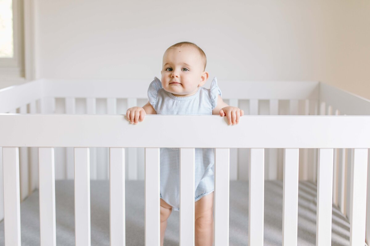 9 month old baby girl standing in white crib smiling