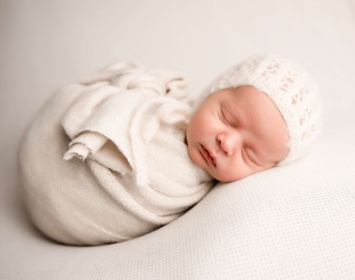 Newborn baby boy wrapped in off-white with a bonnet in a photography studio in Erie Pa