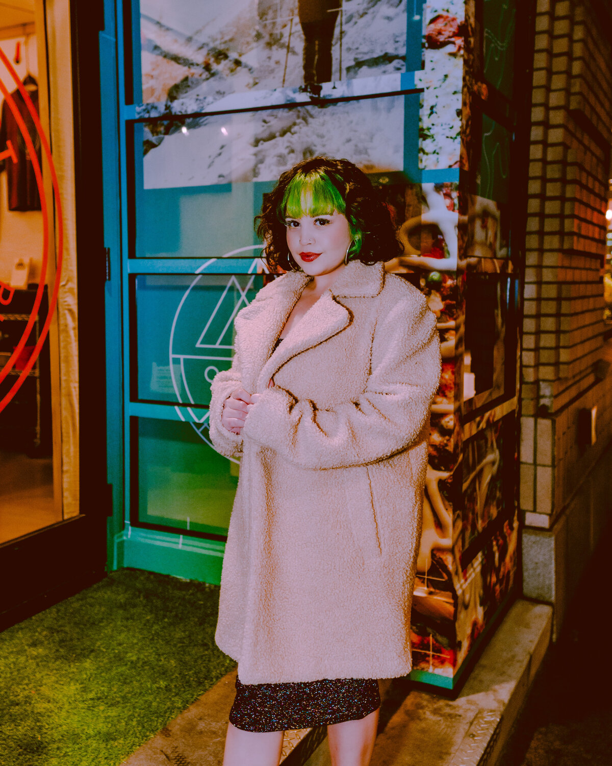 Woman in tan coat standing confidently in front of a neon-lit storefront – bold personal brand image by Mewphotovideo