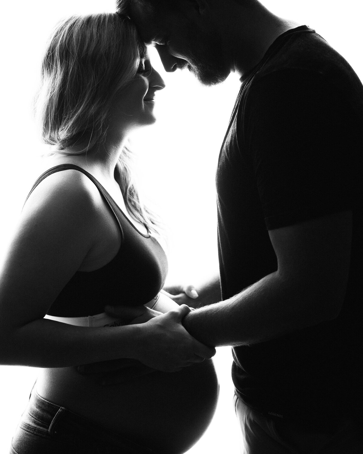 An Iowa maternity photographer image of an expecting couple holding their hands on the bump in silhouette