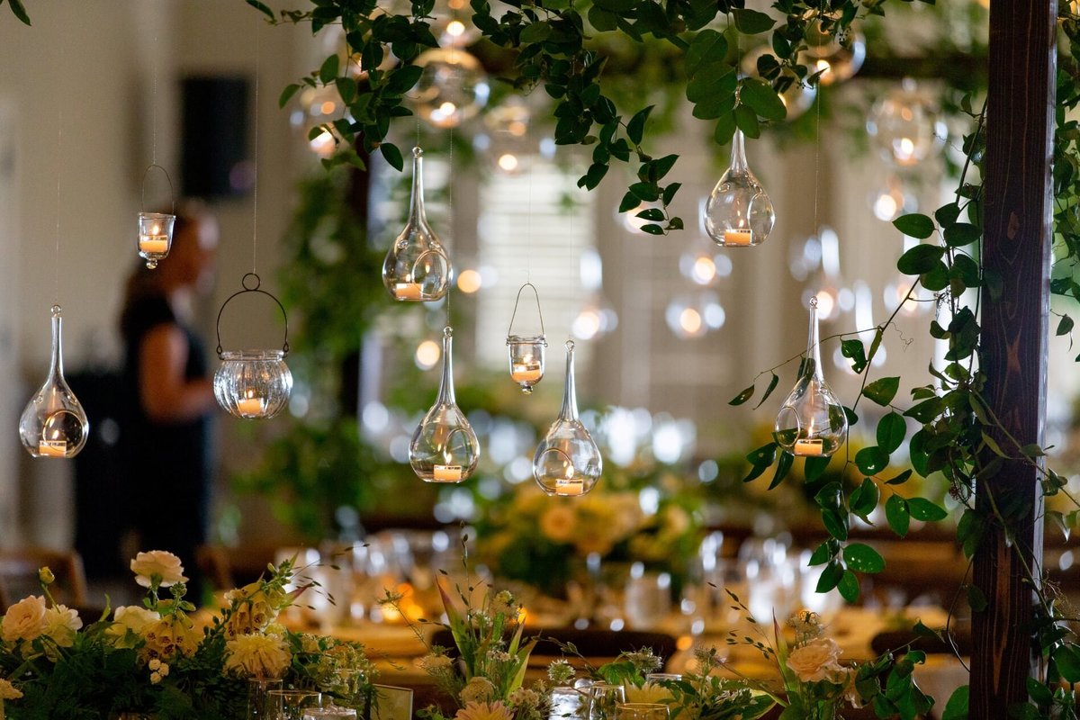 wooden trellis for reception table covered in greenery and decorated with hanging glass candles