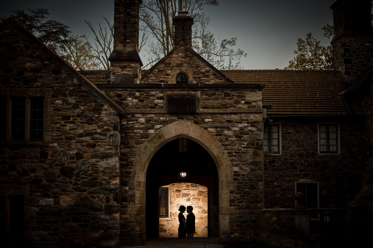 A couple about to kiss while standing under the archway of a stone building.
